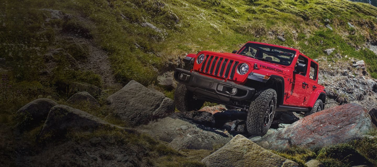 Jeep Wrangler rojo recorriendo un camino de rocas en la montaña
